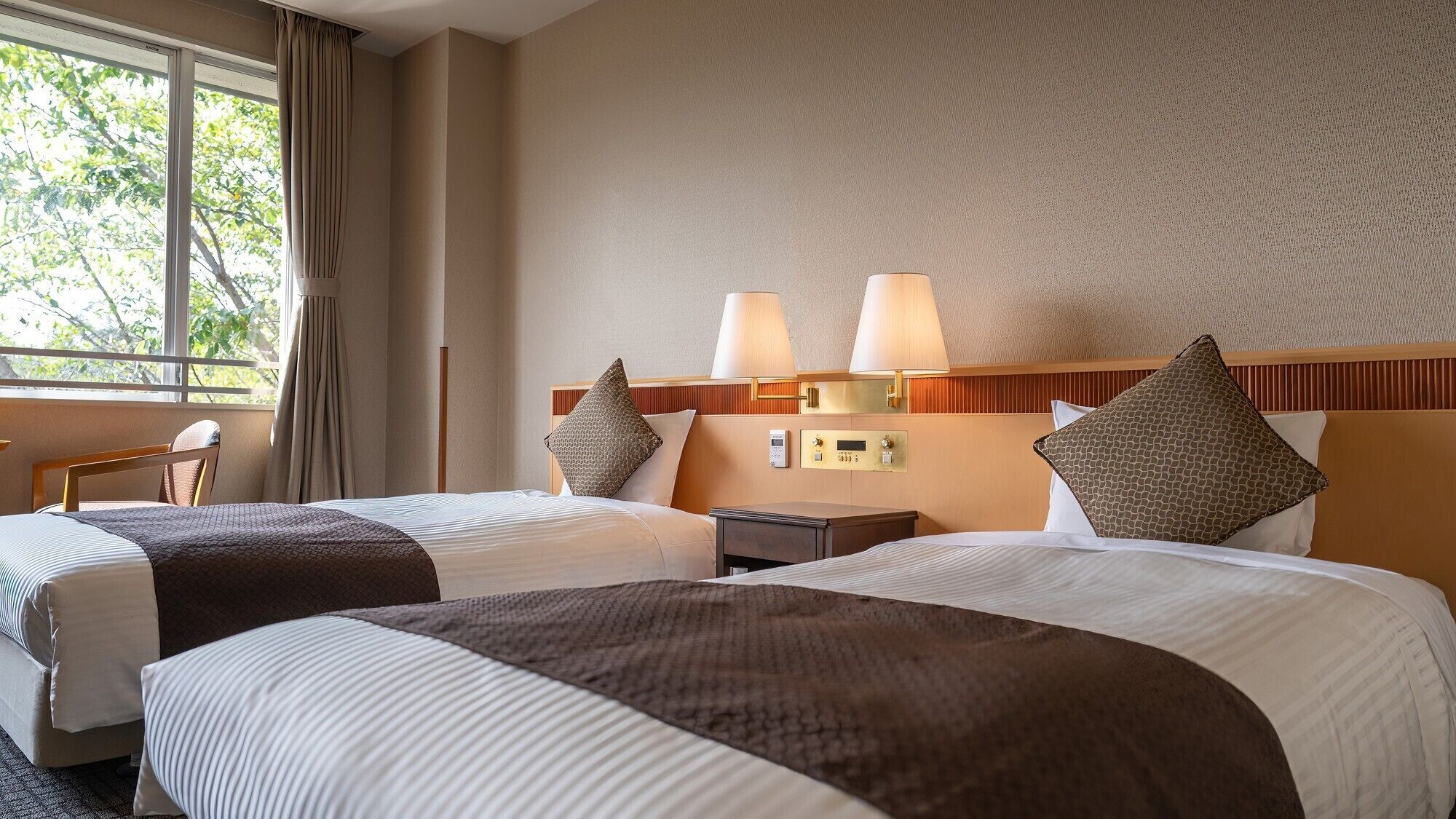 A hotel room with two beds, a nightstand, a desk, and a window with curtains.