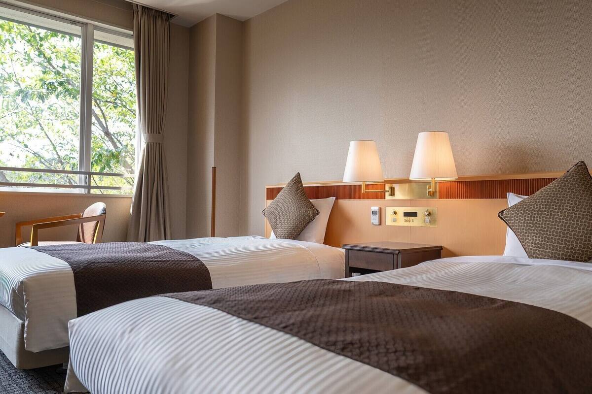 Une chambre d’hôtel avec deux lits, une table de chevet, un bureau et une fenêtre avec des rideaux.