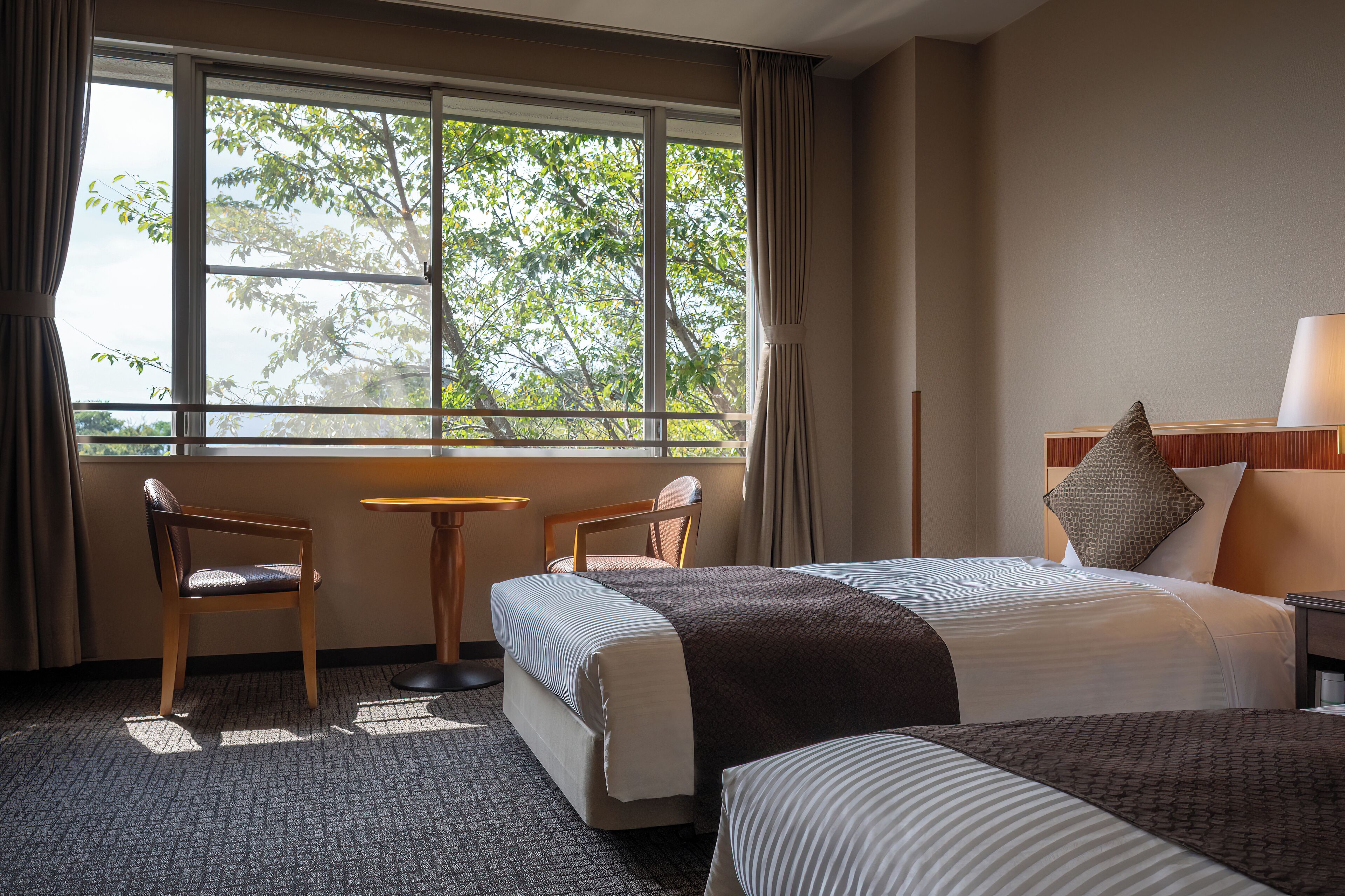 A hotel room with a bed, two chairs, a small table, and a window with curtains.