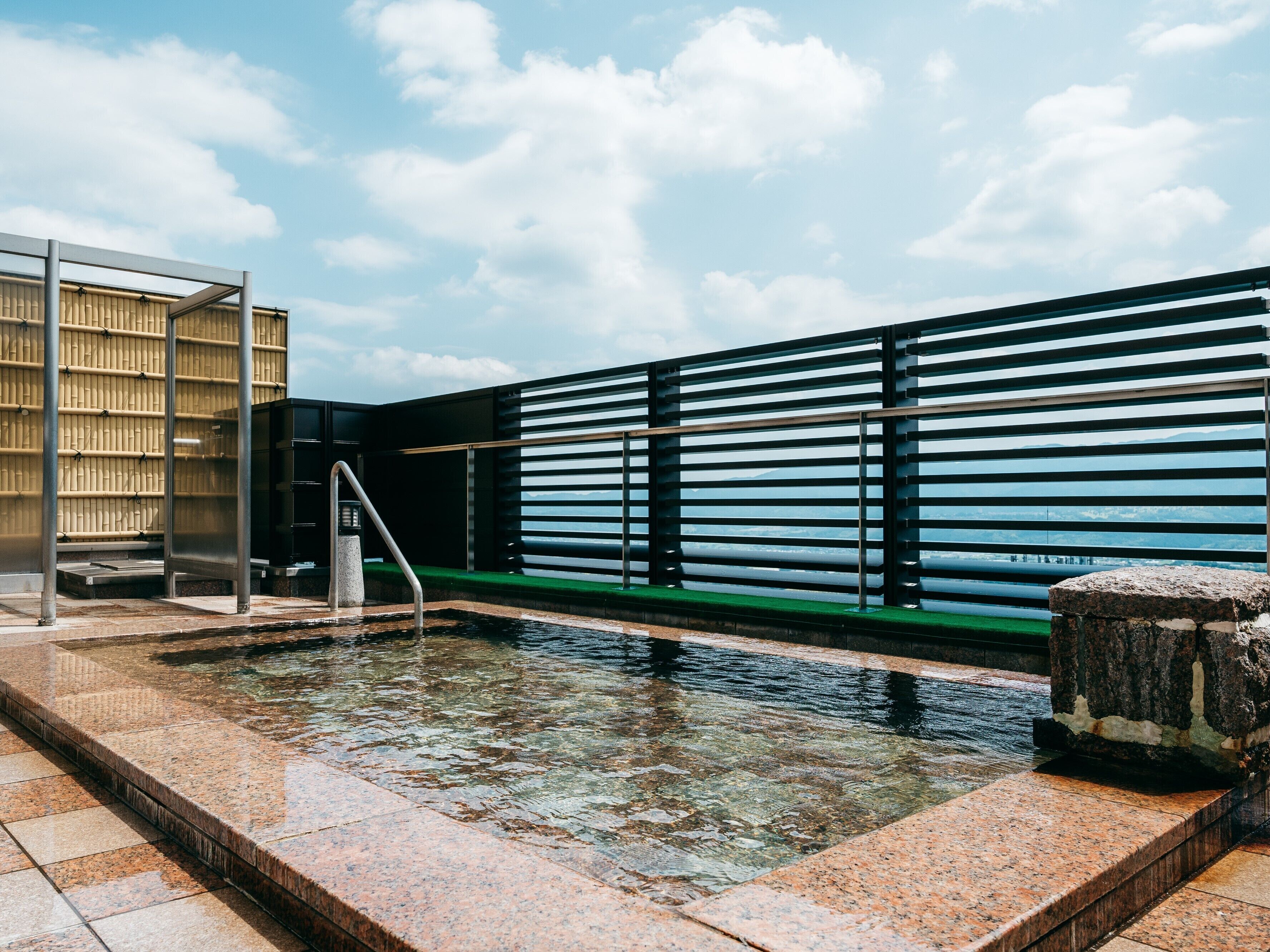 A pool area with clear water, a stone structure, and a metal railing.