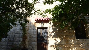 Un edificio de piedra con puerta de madera, plantas en macetas y un toldo rojo.