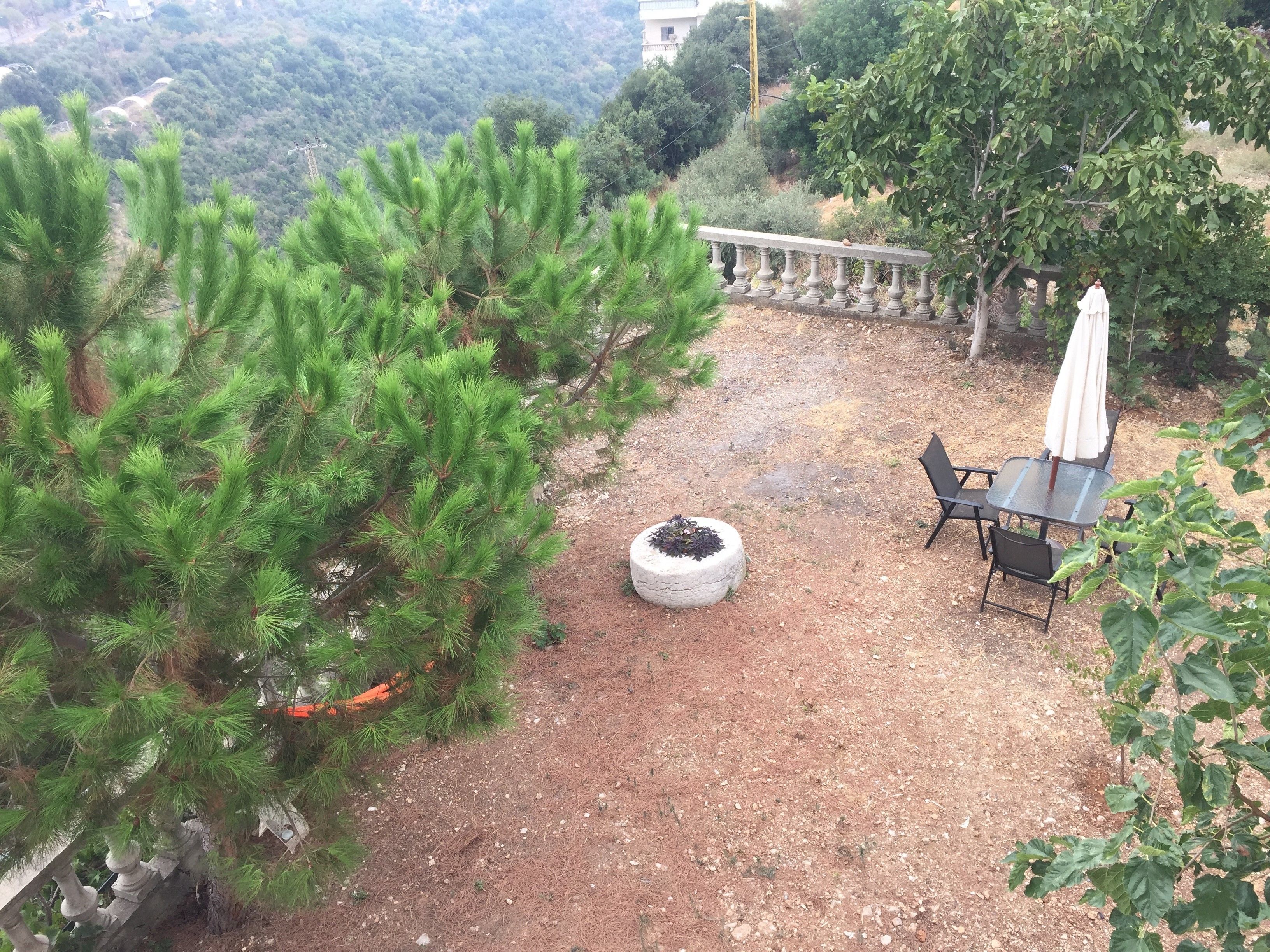 A patio area with a stone table and chairs, surrounded by greenery and a stone balustrade.