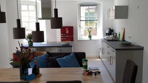 Une cuisine moderne avec un coin repas, comprenant une table en bois, des chaises, des luminaires suspendus et un réfrigérateur rouge.