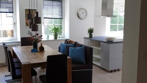 Une cuisine moderne avec un coin repas, comprenant une table en bois, des chaises noires, un canapé noir avec des coussins bleus et une horloge au mur.