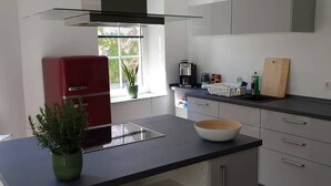 Une cuisine moderne dotée d’un îlot central, d’un réfrigérateur rouge et d’une fenêtre donnant sur un paysage verdoyant.