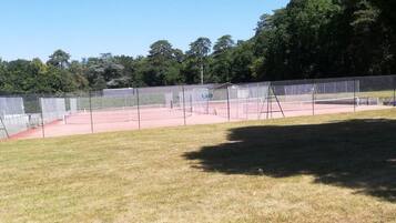 Una cancha de tenis con una red, rodeada por una cerca de malla y árboles al fondo.