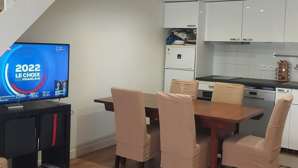 Un salon moderne avec un coin repas, un plancher en bois, un escalier et une cuisine en arrière-plan.