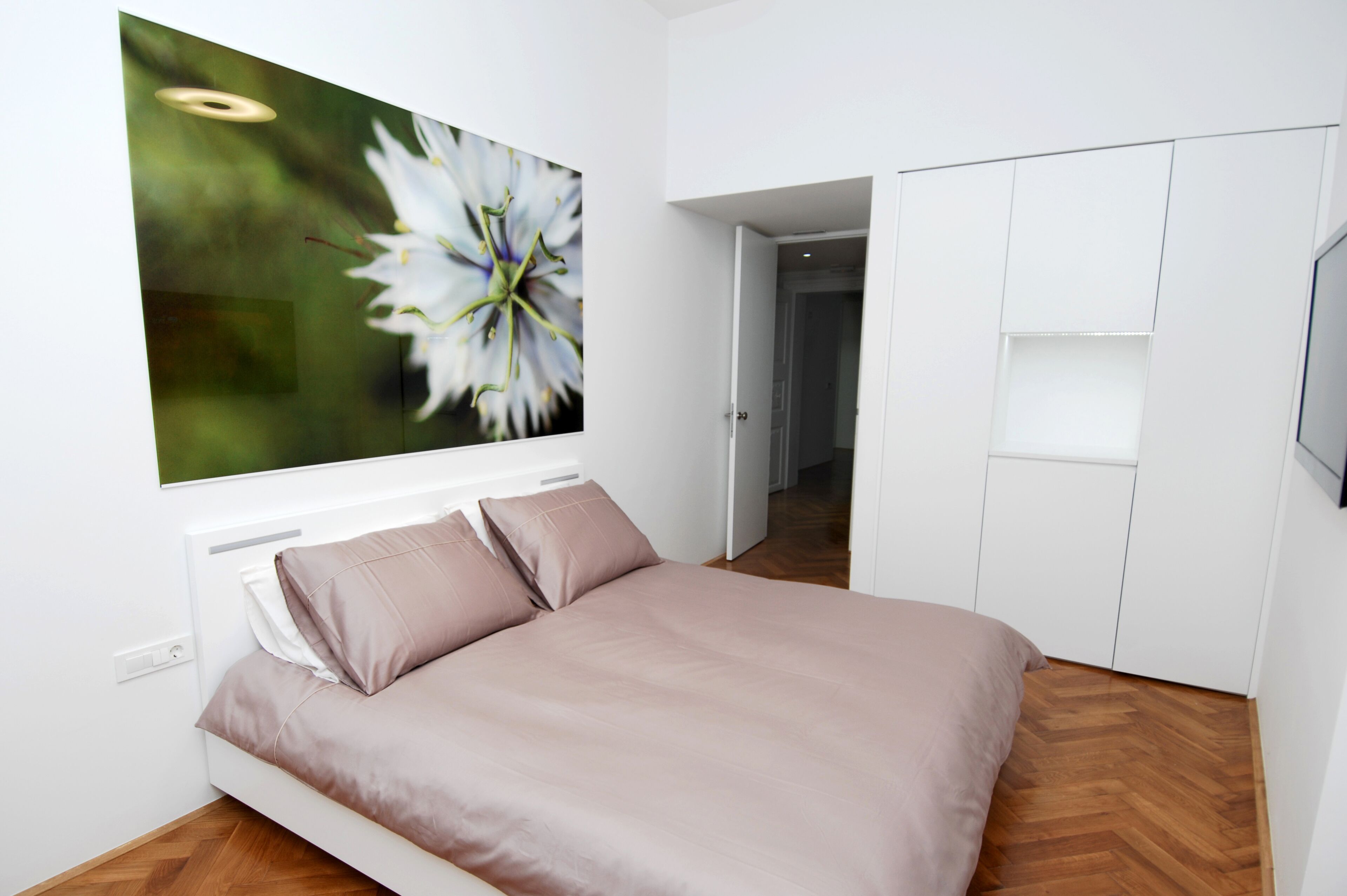 A bedroom with a bed, a white wardrobe, and a large window with a flower painting.