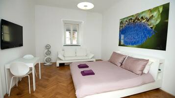 A modern bedroom with a bed, a desk, a chair, a TV, and a window.