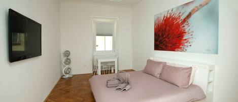 A modern bedroom with a large bed, a flat-screen TV, a desk, and a chair.