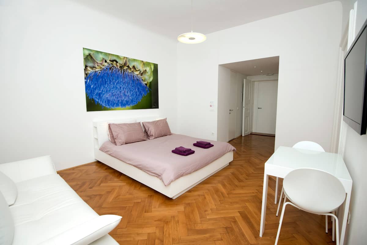 Une chambre à coucher moderne avec un lit, des chaises blanches, une petite table et un tableau au mur.