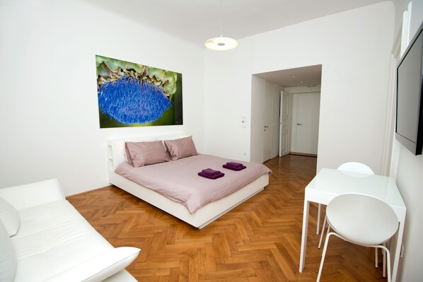Ein modernes Schlafzimmer mit einem Bett, weißen Stühlen, einem kleinen Tisch und einem Bild an der Wand.