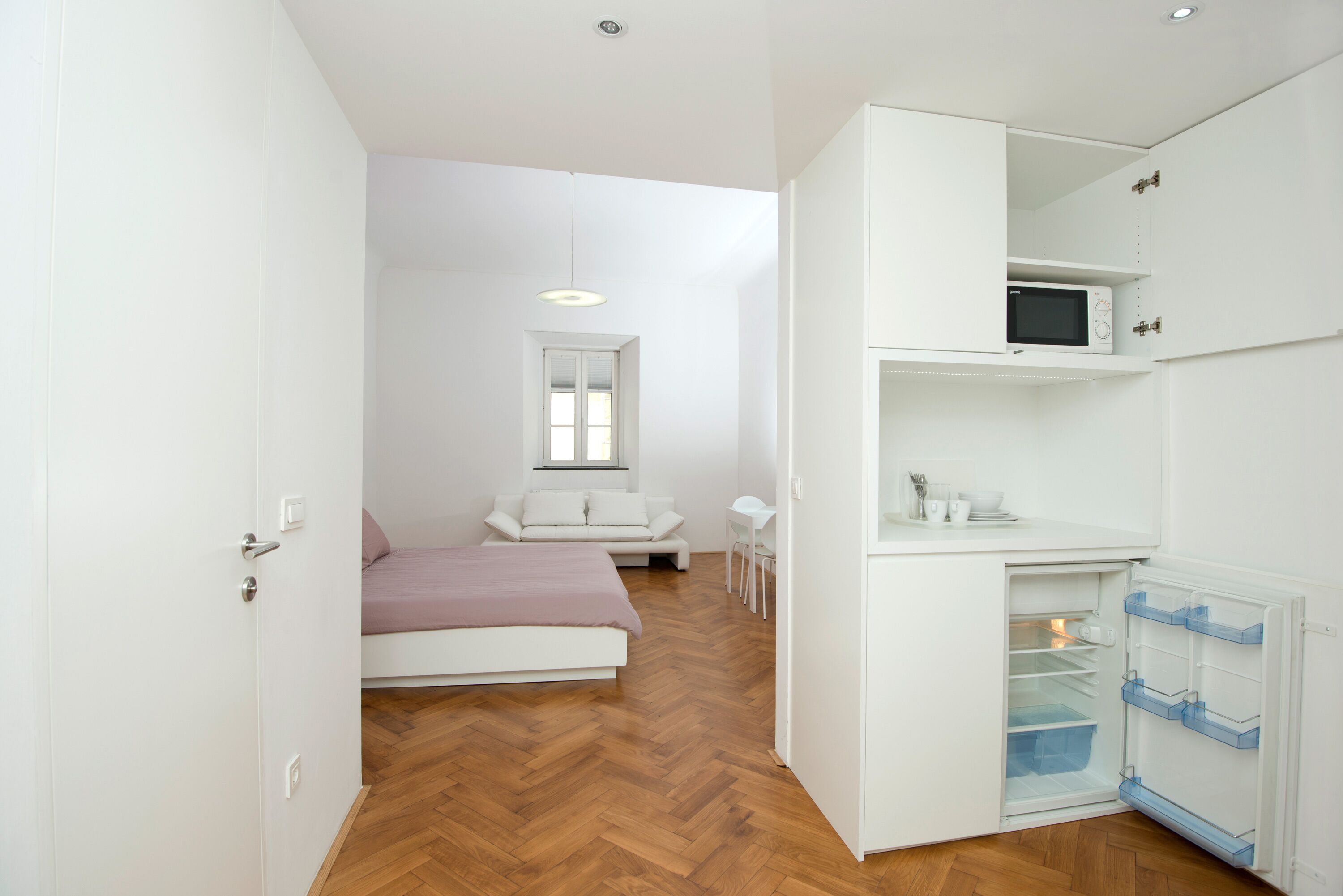 Ein kleines Schlafzimmer mit einem Bett, einem Schreibtisch und einem weißen Kleiderschrank mit integriertem Mikrowellenherd.