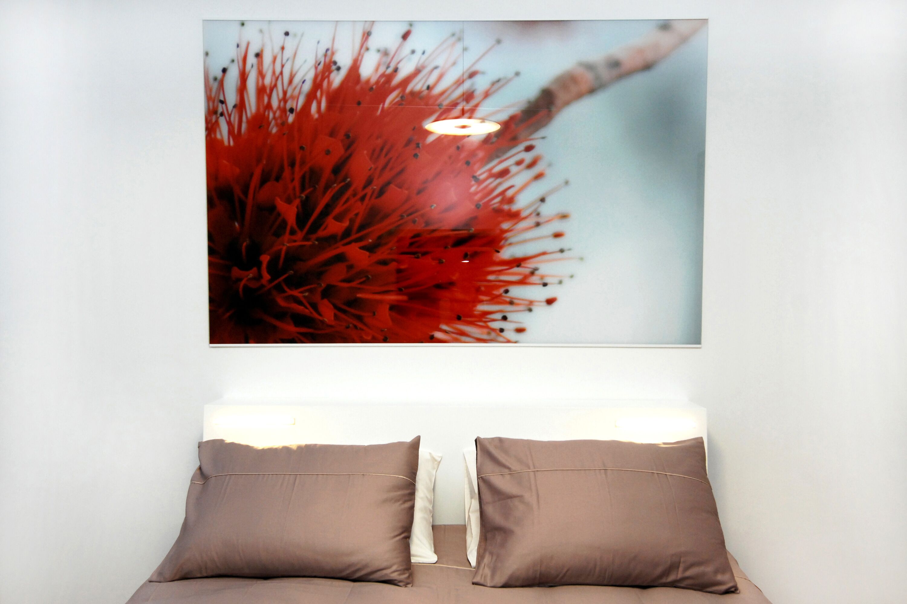 A bedroom with a bed, two pillows, and a wall-mounted artwork of a red flower.