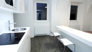 Une cuisine moderne dotée d’un four à micro-ondes encastré, d’un évier en acier inoxydable et d’une plaque de cuisson à induction noire. On y trouve deux tabourets de bar blancs et une fenêtre qui laisse entrer la lumière naturelle.