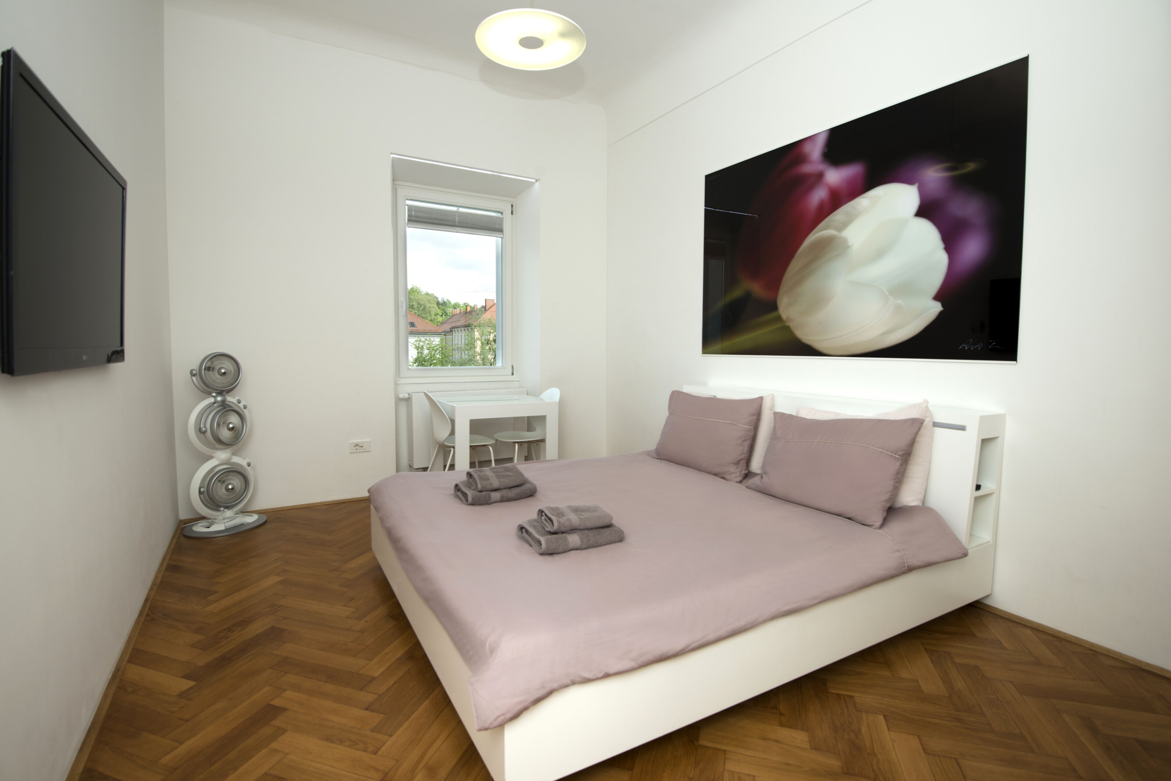 A bedroom with a bed, a desk, and a large window.
