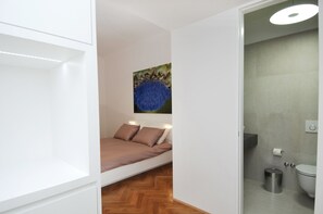 Ein Schlafzimmer mit Bett, einem Gemälde, einer Toilette und einem Mülleimer.