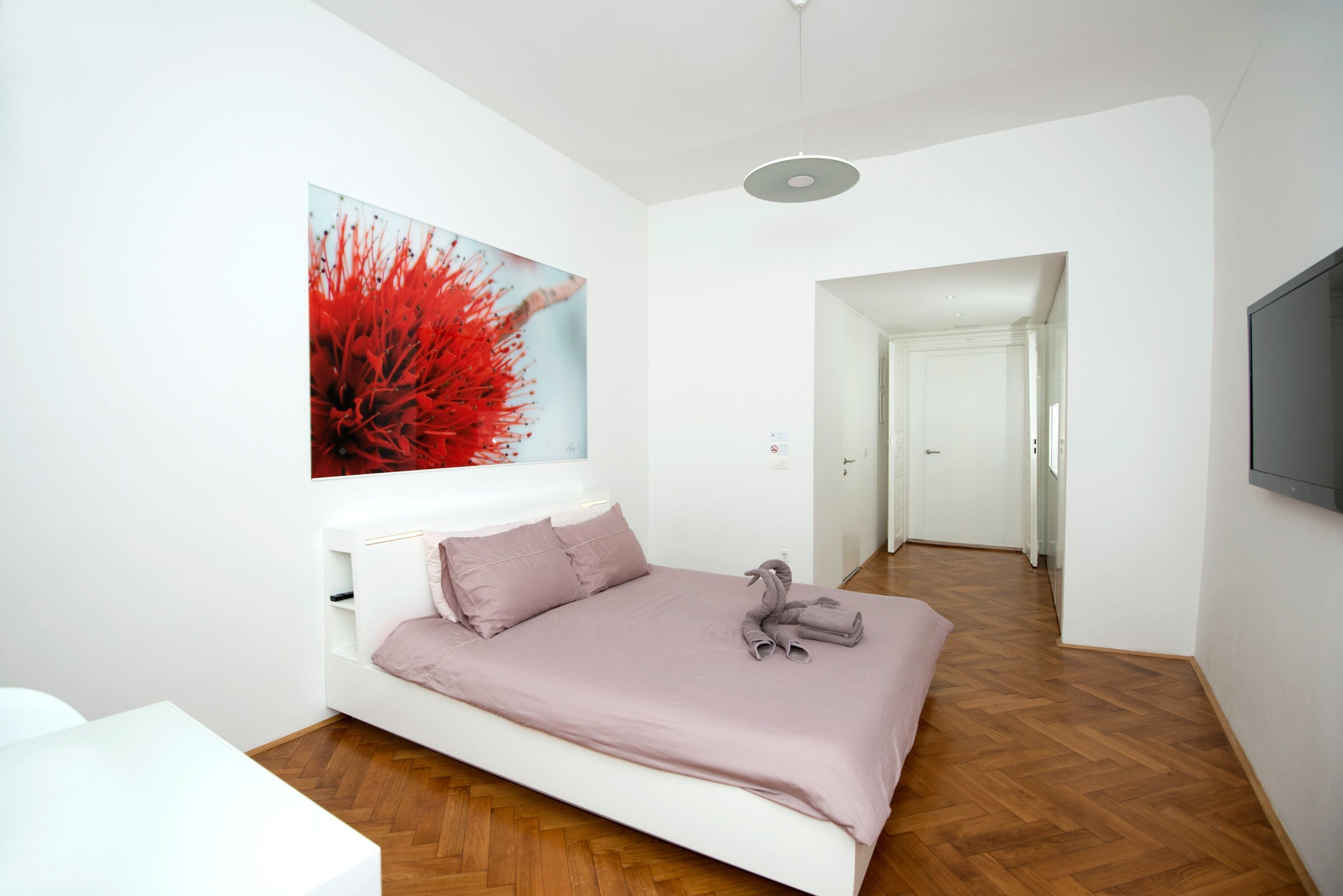 Una camera da letto moderna con un letto bianco, un grande quadro floreale rosso e un pavimento in legno.