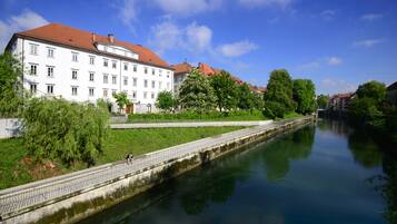 A river with a bridge, a white building with a red roof, and green trees.