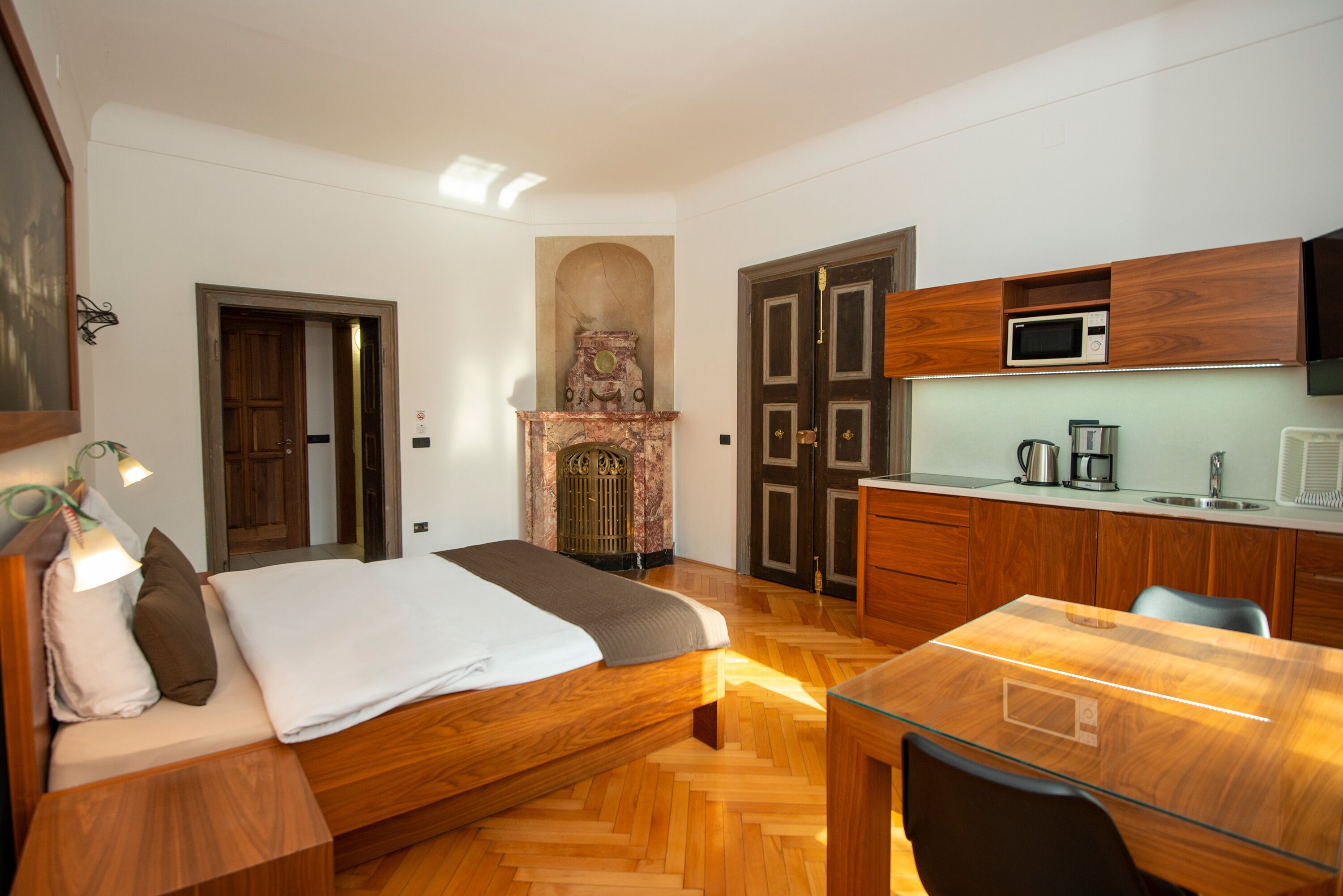 Ein Schlafzimmer mit einem hölzernen Bett, einem Glastisch, einer Küchenzeile mit Mikrowelle und einem Kamin.