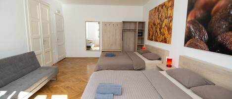 A hotel room with two beds, a sofa, a wardrobe, and a large wall painting.