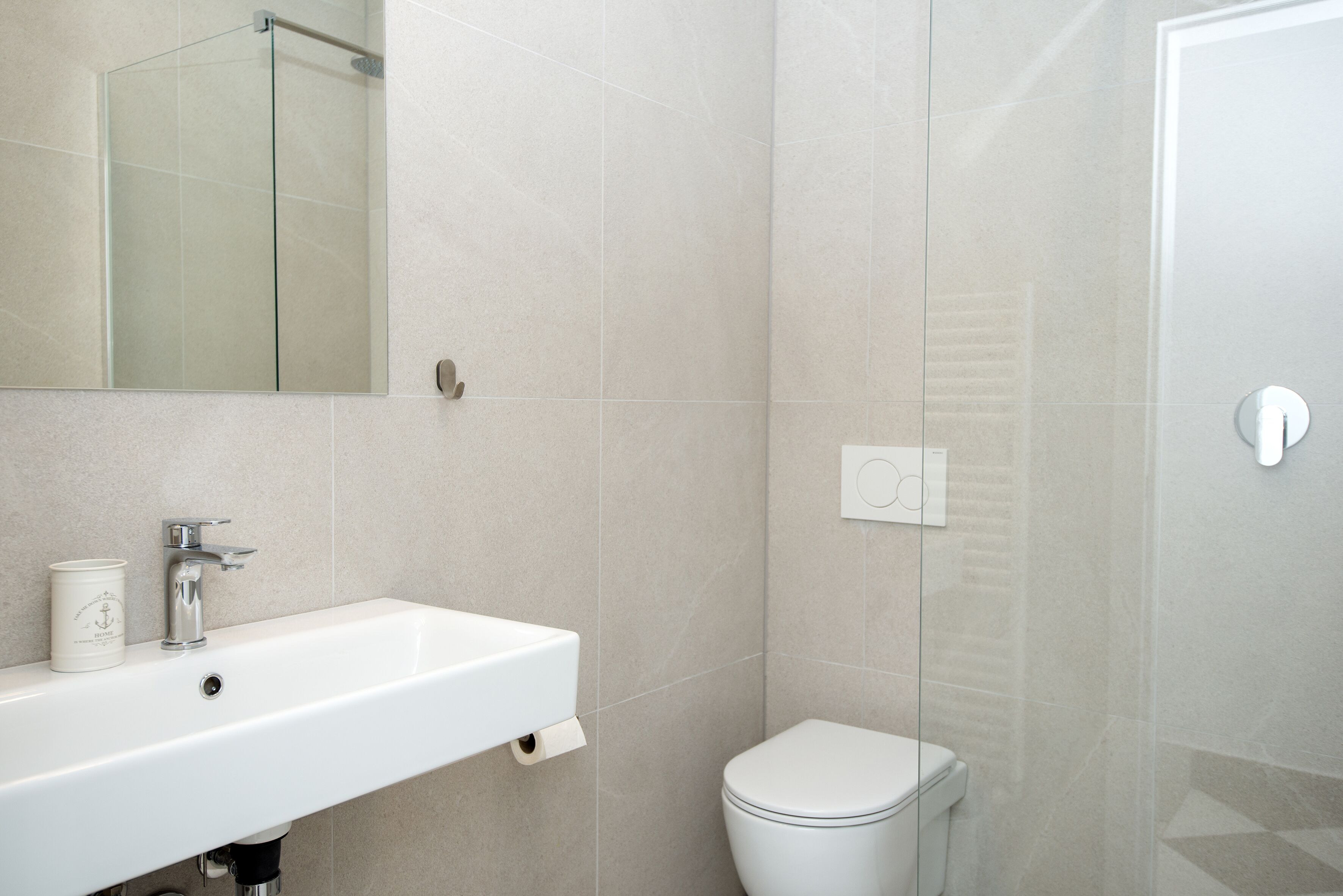 Une salle de bain avec un lavabo blanc, un miroir, des toilettes et une cabine de douche en verre.
