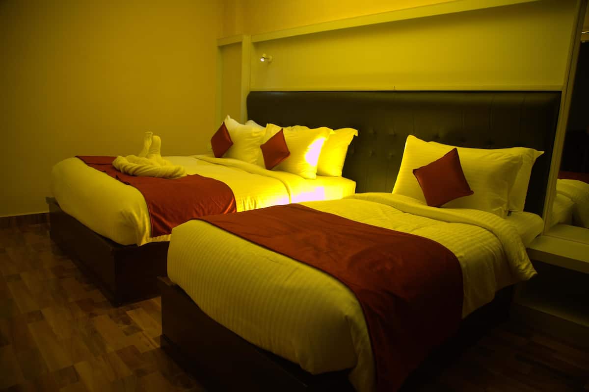 Habitación de hotel con dos camas, cada una con cabecero y varios almohadones.