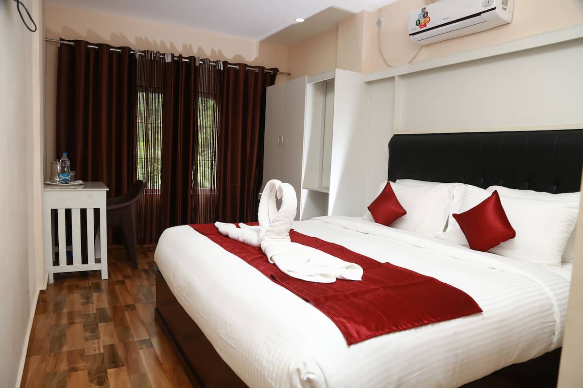 Habitación de hotel con una cama bien hecha, un escritorio pequeño con una botella de agua, un armario y un equipo de aire acondicionado.