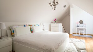 A bedroom with a large bed, a bedside table with a lamp, a dresser, a small table with a mirror, and a chandelier. - VIP Apartment (Ljubljana)