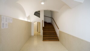 A staircase in a building with white walls and a tiled floor. There is a door at the top of the stairs and a sign on the wall to the left. - VIP Apartment (Ljubljana)