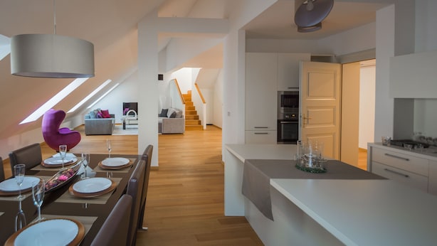 A modern kitchen with white cabinetry, a central island, and a dining area with a table set for four. - VIP Apartment (Ljubljana)