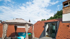 A rooftop terrace with a blue sofa, a pergola, and a glass door leading to a bedroom. - VIP Apartment (Ljubljana)