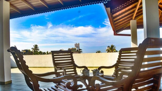 A covered outdoor seating area with two wooden chairs and a small table, featuring a clear view of the sky and distant buildings. - Southern Coastal Villas (Hikkaduwa)