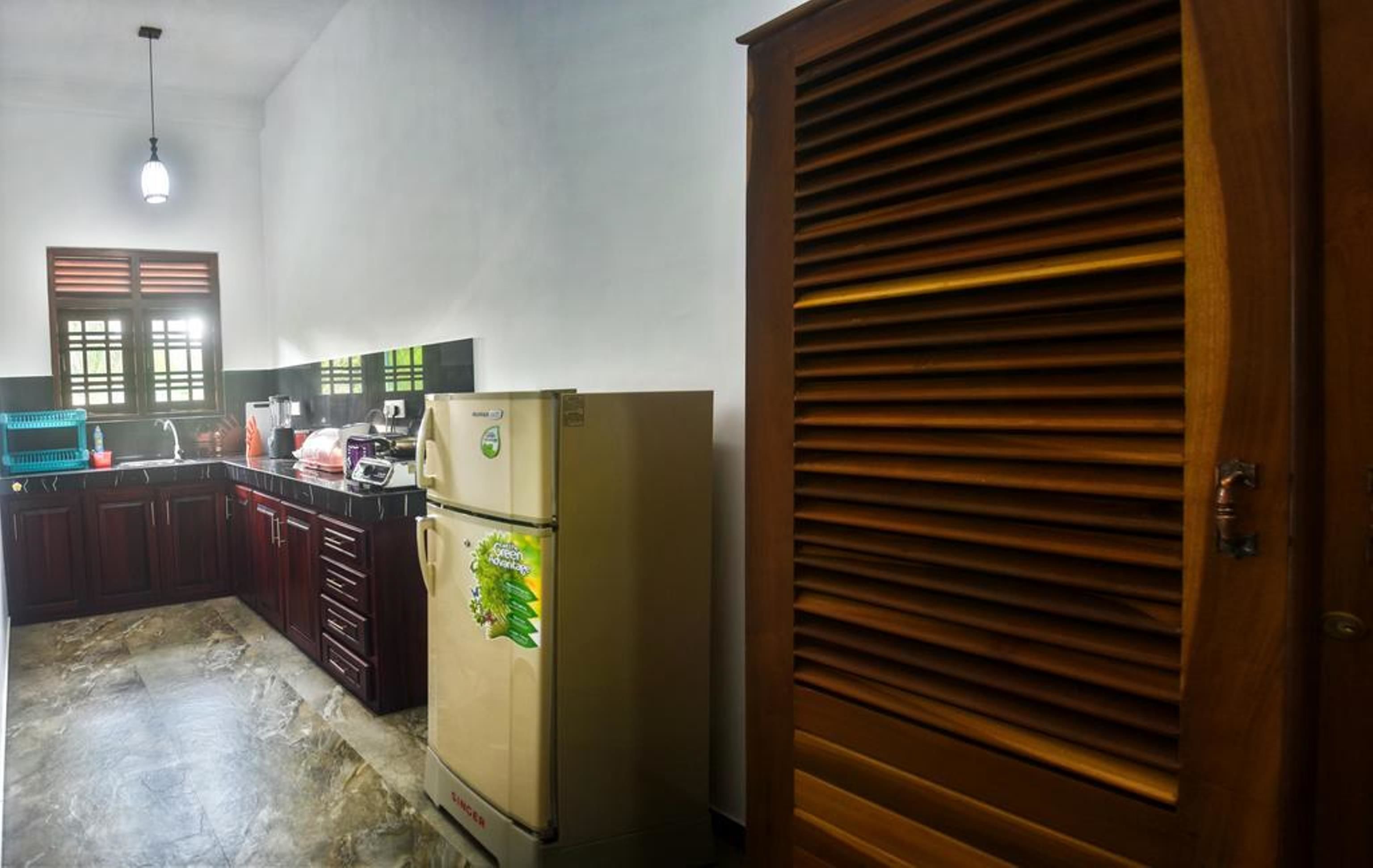 A kitchen with a refrigerator, cabinets, and a window with blinds.