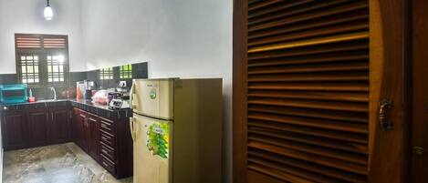 A kitchen with a refrigerator, cabinets, and a window with blinds.