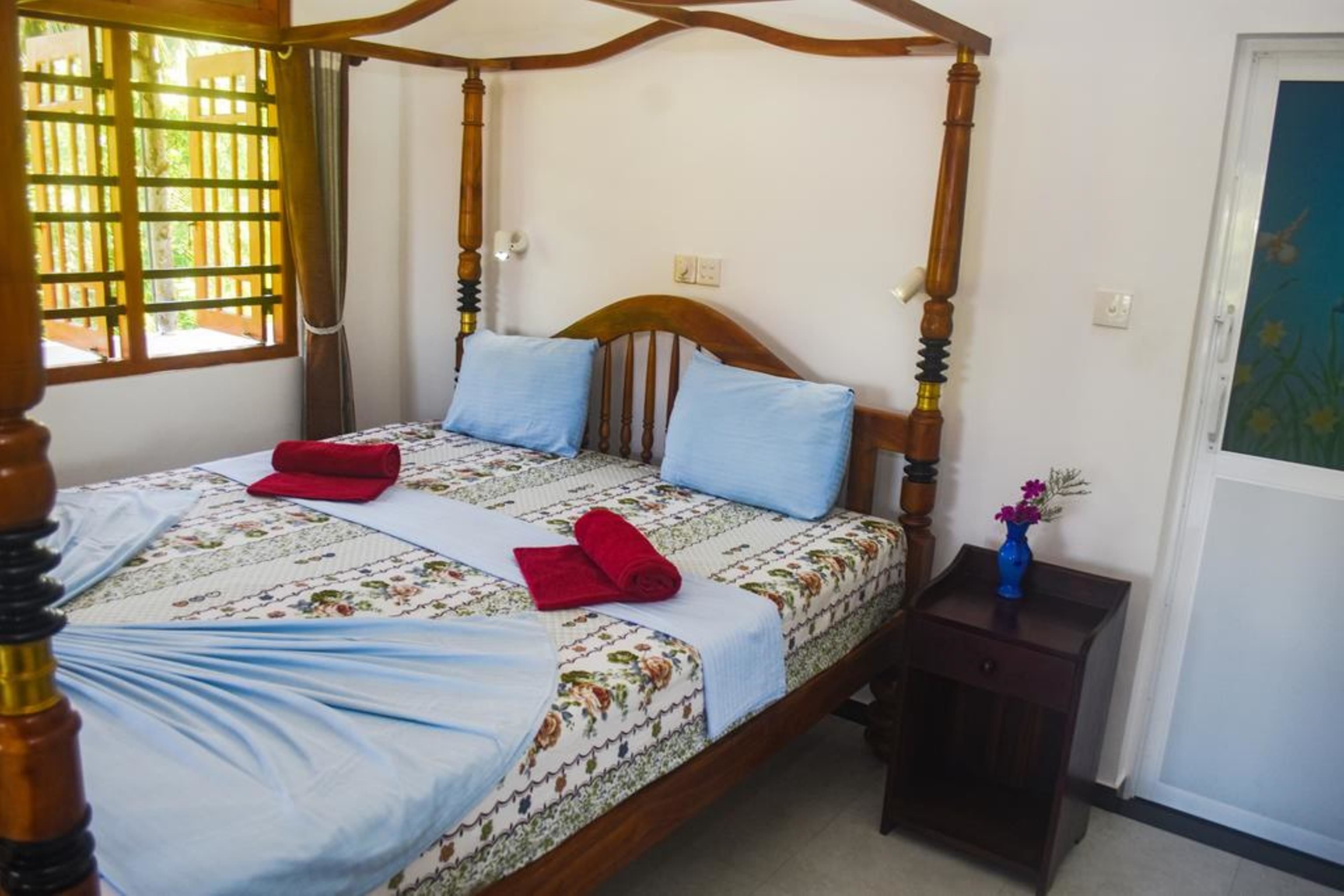 A four-poster bed with a floral bedspread, two pillows, and a small bedside table with a vase.