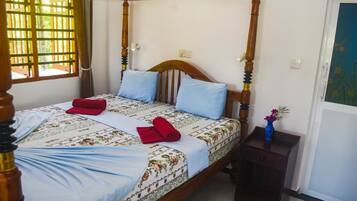 A four-poster bed with a floral bedspread, two pillows, and a small bedside table with a vase.