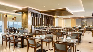 A modern dining area with multiple tables and chairs, a bar, and a view of the mountains. - Hotel Santika Gresik (Gresik)