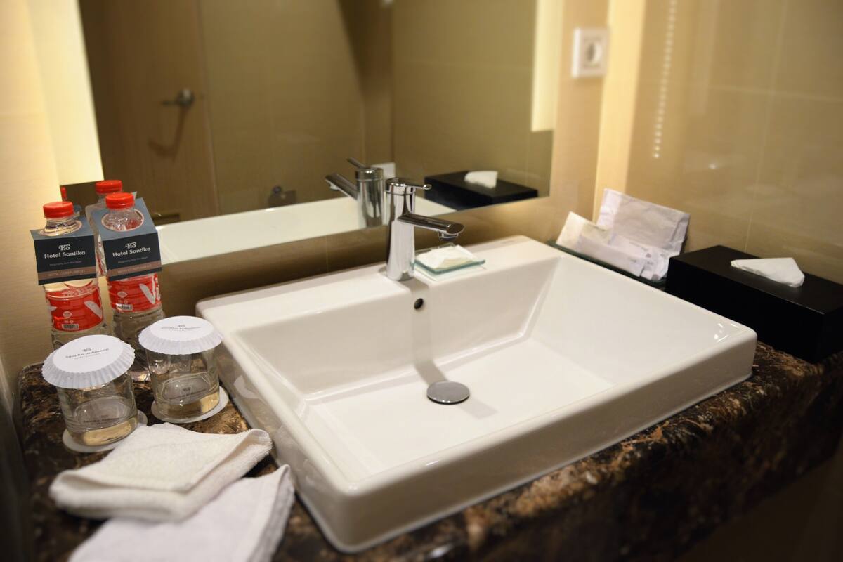 A hotel bathroom with a large white sink, a mirror, and toiletries including bottles and a towel.