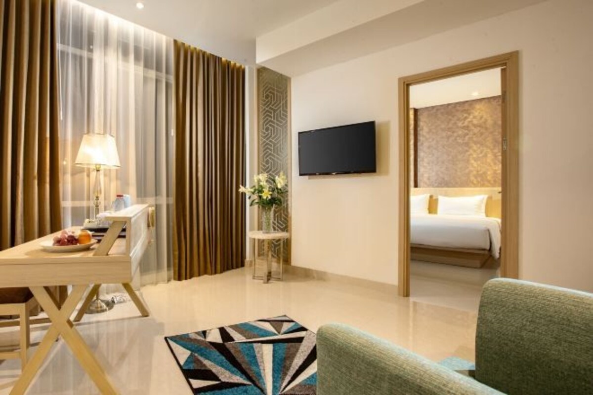 Habitación de hotel con cama, televisión montada en la pared, escritorio con lámpara y una pequeña mesa con flores.