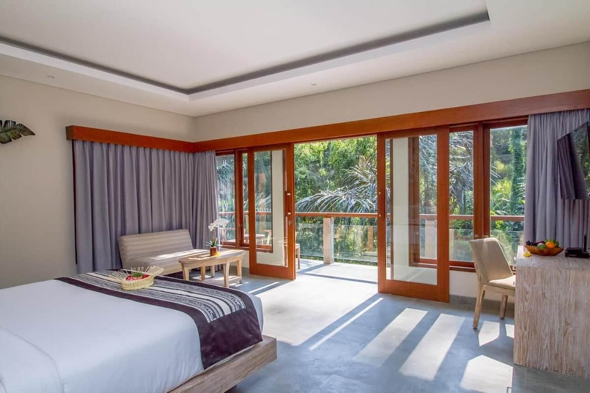 Ein modernes Hotelzimmer mit einem großen Bett, einem kleinen Tisch und einem Balkon mit Blick auf Grünflächen.