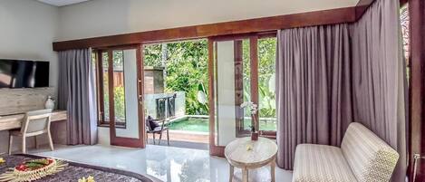 A spacious bedroom with a large bed, a desk, a TV, and a balcony with a pool.