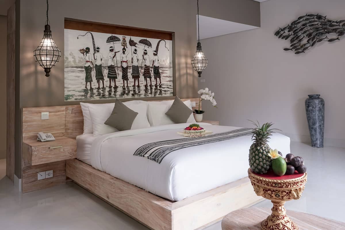 Ein modernes Schlafzimmer mit einem Holzbettrahmen, einem Gemälde über dem Bett, einer Obstschale auf dem Nachttisch und einer Vase am Boden.
