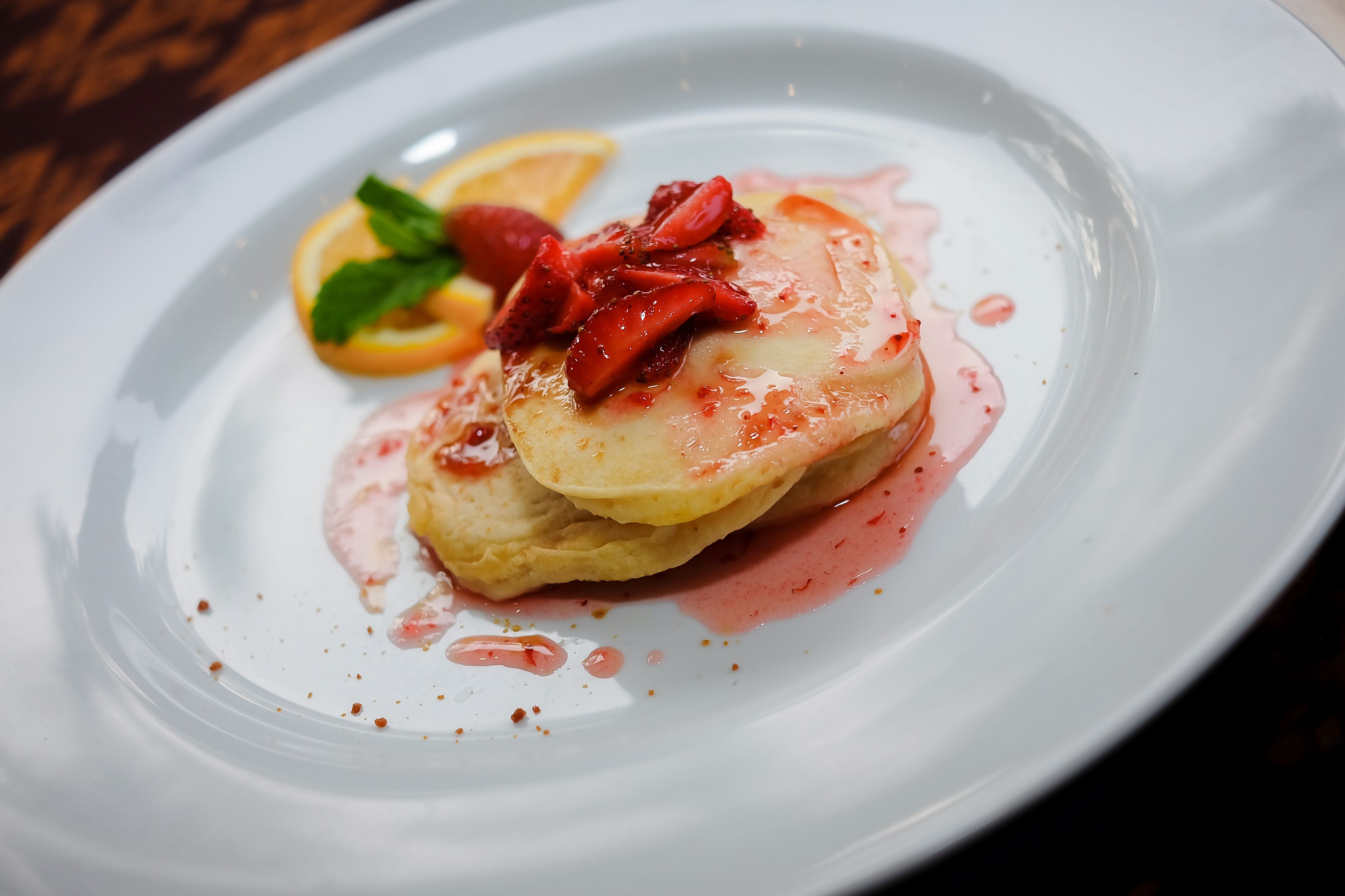 A dessert plate with pancakes, strawberries, and a mint leaf.