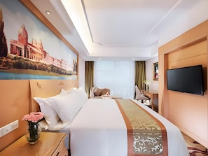 Een hotelkamer met een groot bed, een bureau, een stoel, een televisie en een schilderij aan de muur.