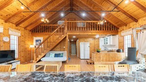 Une vaste cabane en bois dotée d’un plafond haut, d’un escalier central, d’un coin cuisine et d’un espace salon avec une table en marbre.
