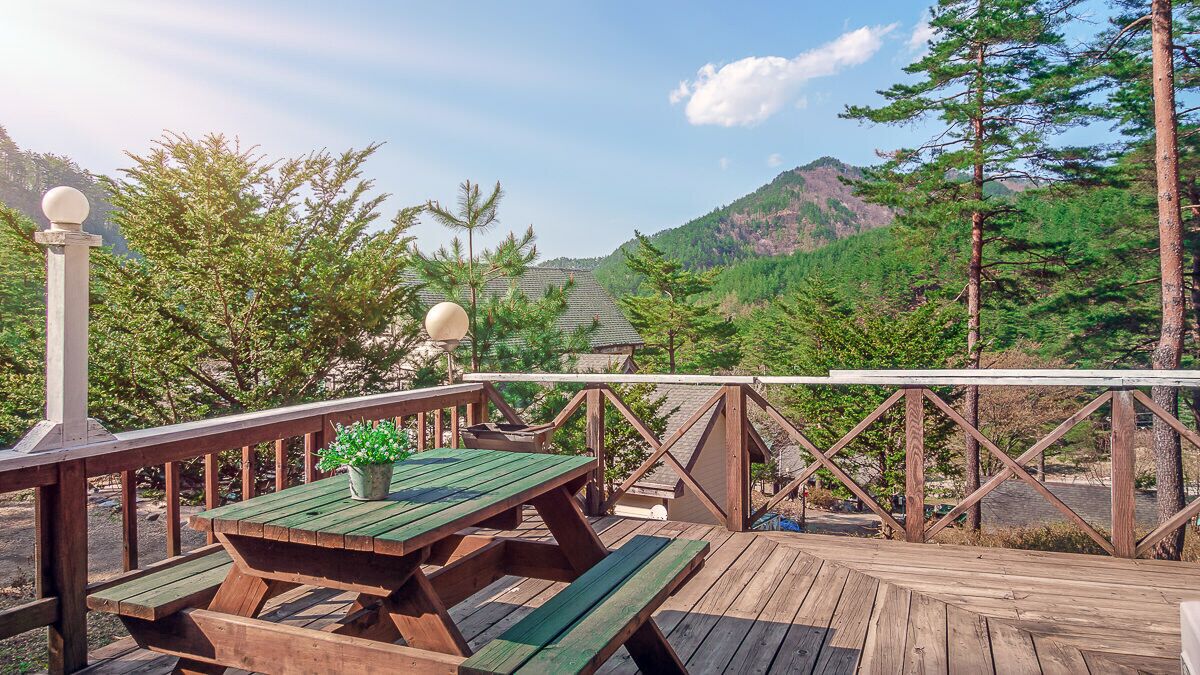 Um deck de madeira com mesas de piquenique e vista para uma cordilheira arborizada.