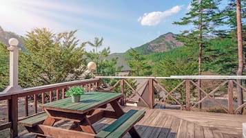 Um deck de madeira com mesas de piquenique e vista para uma cordilheira arborizada.