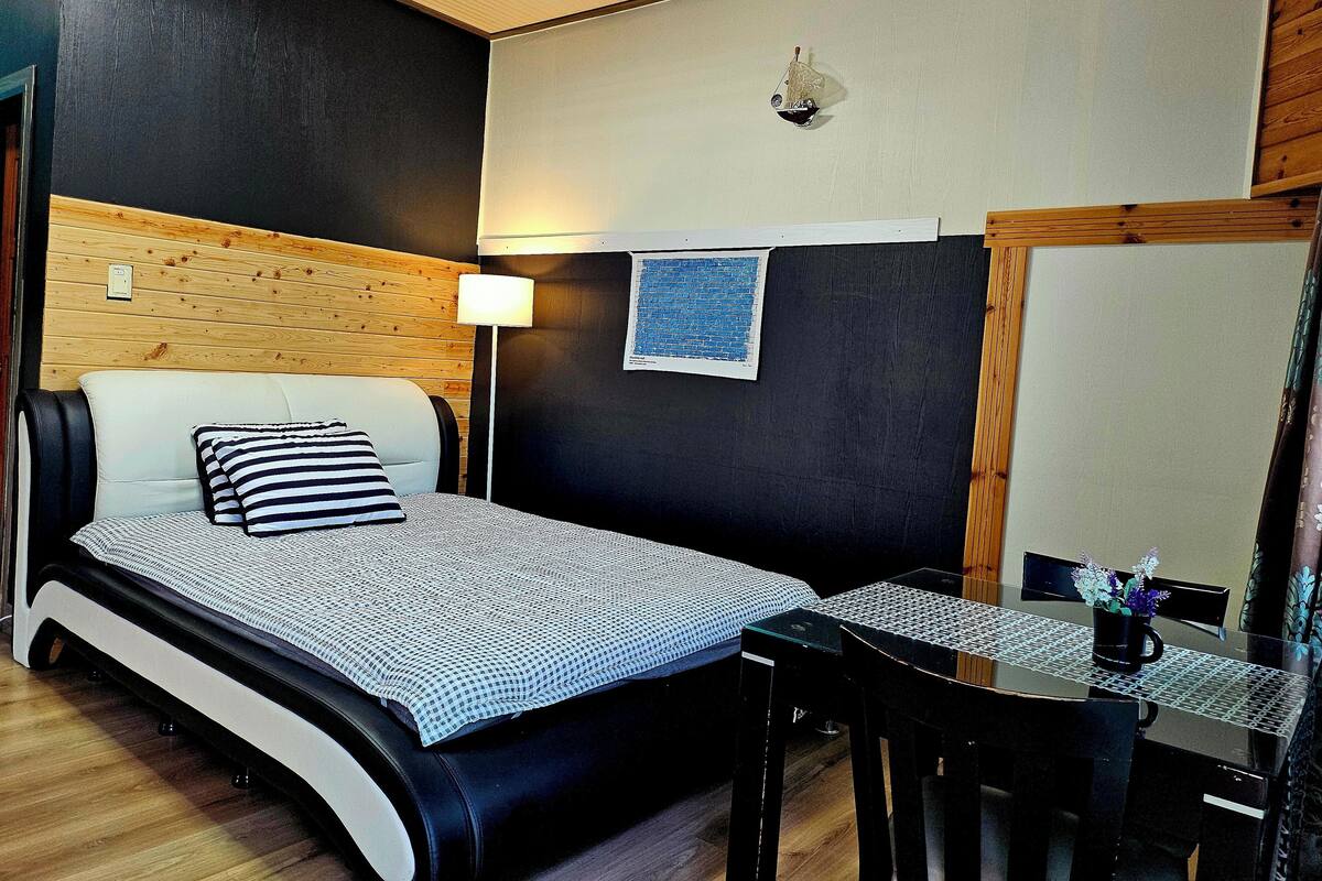 A bedroom with a bed, bedside table, lamp, and a small table with chairs.