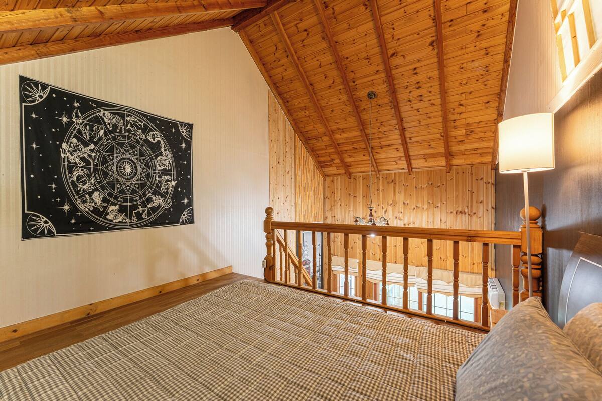 A room with a wooden ceiling, a checkered floor, a wooden railing, and a wall tapestry.